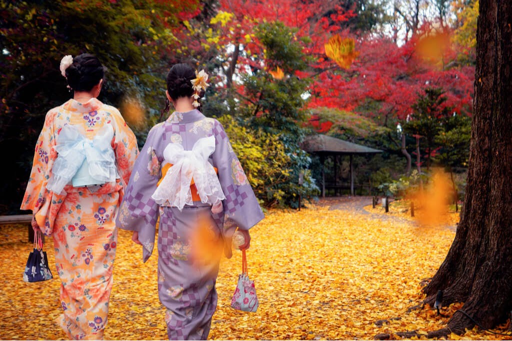 Two women in kimonos walk through a park in Tokyo with beautiful changing leaves
