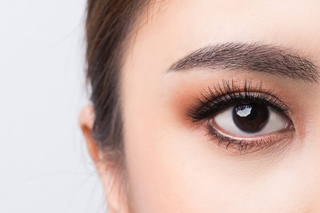 A woman's eye with long lashes and a slightly orange eye shadow