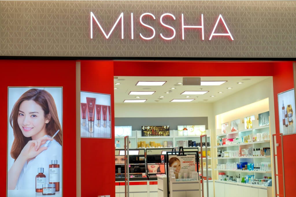 The exterior of a small MISSHA store with an ad with a woman holding a product outside