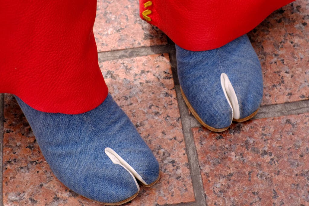 A woman standing with the photo focused on her blue camel toe shoes  with her red pants in the photo too