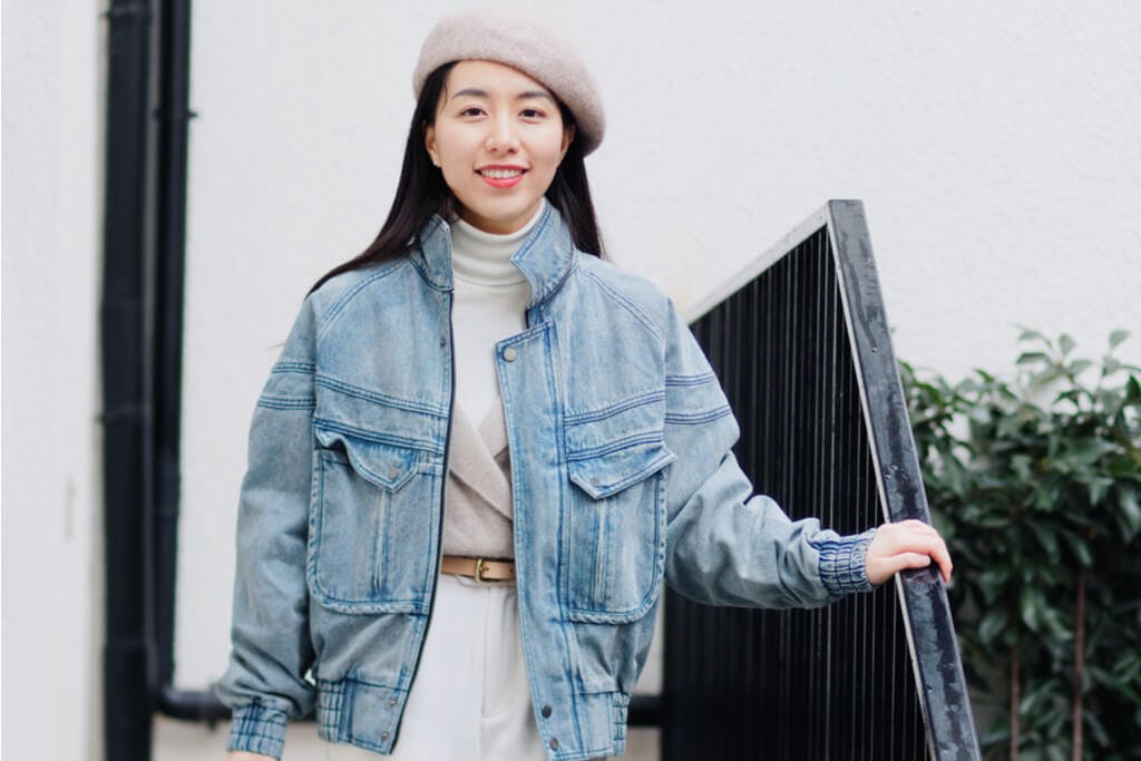 A young Korean woman wearing a Korean Fall Fashion outfit of a denim jacket, sweater, pants and beret while standing on stairs
