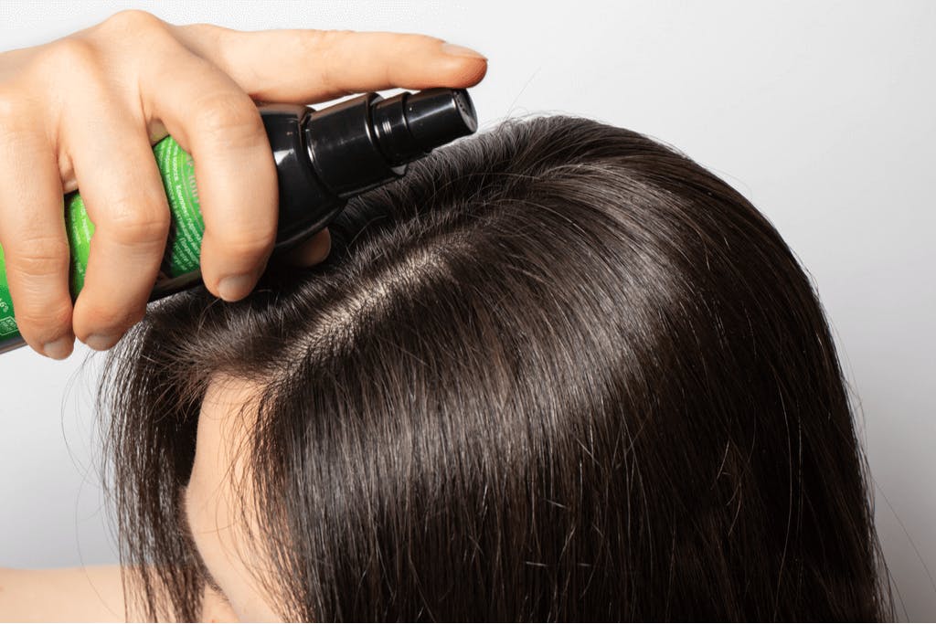 A woman applies a hair tonic, a must-have Japanese hair care product, to her scalp among her shiny hair.