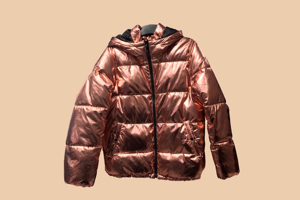 A gold metallic puffer jacket, a popular Japanese fall fashion choice, on a brown background. 