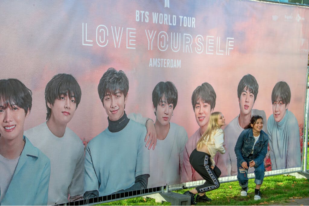 Two young women pose in front a BTS World Tour Billboard
