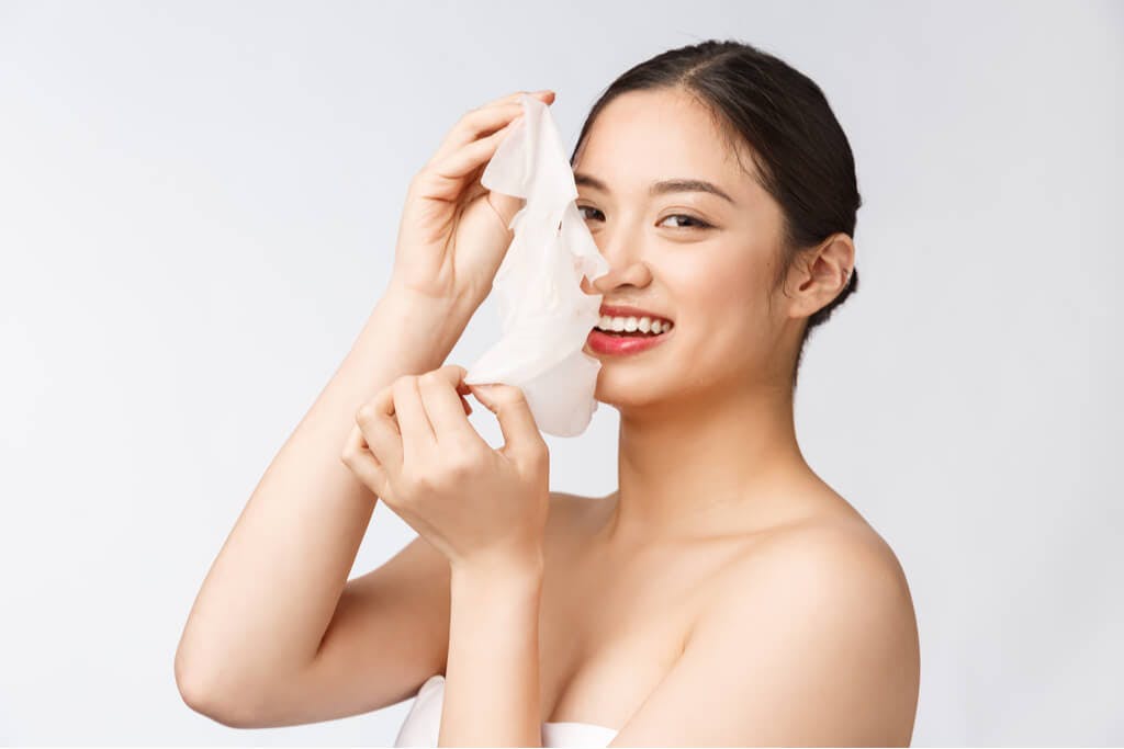 A woman smiling while taking off a Japanese sheet mask and revealing nice skin underneath