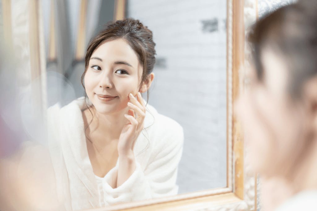 A woman appreciates her skin in the mirror after cleansing and moisturinzing her skin with Japanese cosmetics