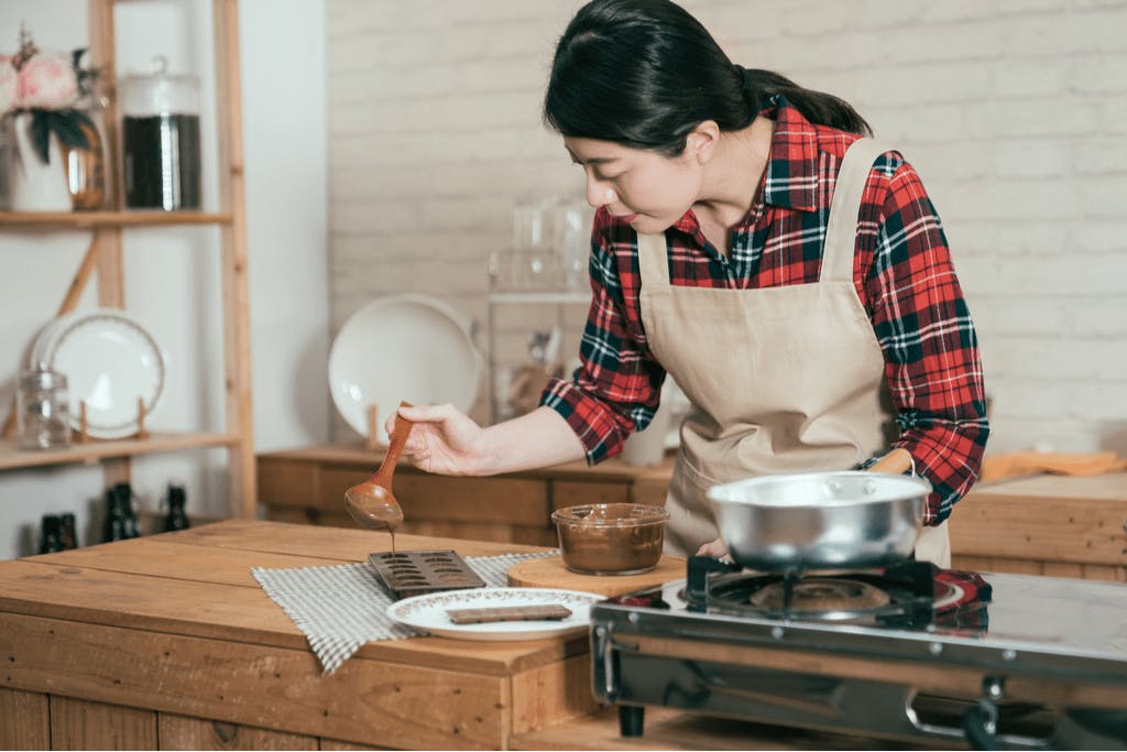 A woman in a kitchen, wearing an apron, spoons chocolate into a mold to create a gift for Valentine's Day in South Korea.