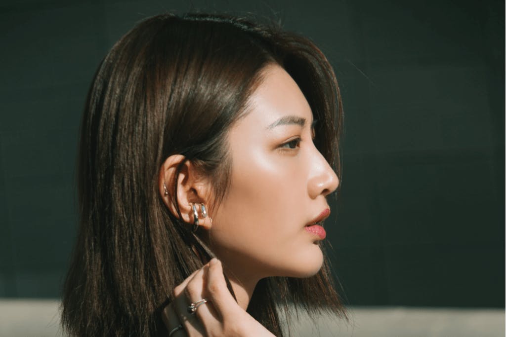 A beautiful Korean woman in Seoul wearing full makeup brushes her long, shiny hair behind her ear.
