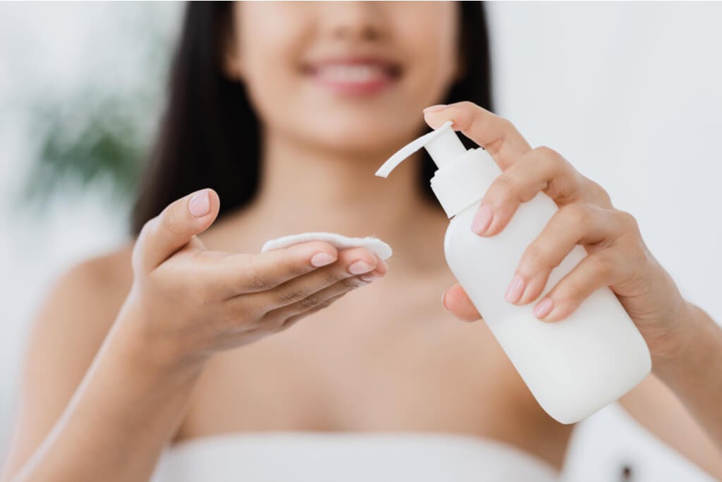 A woman applies Japanese lotion to a pad in her hand as she smiles towards the camera