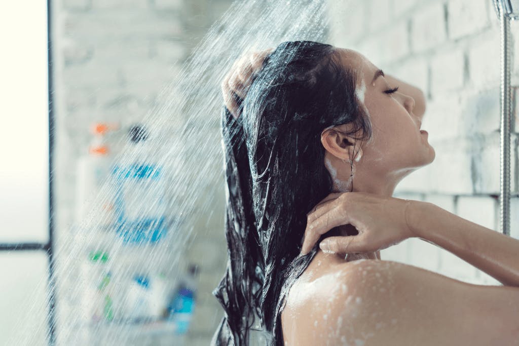 A woman showers in large shower and rinses Japanese hair shampoo out of her hair.