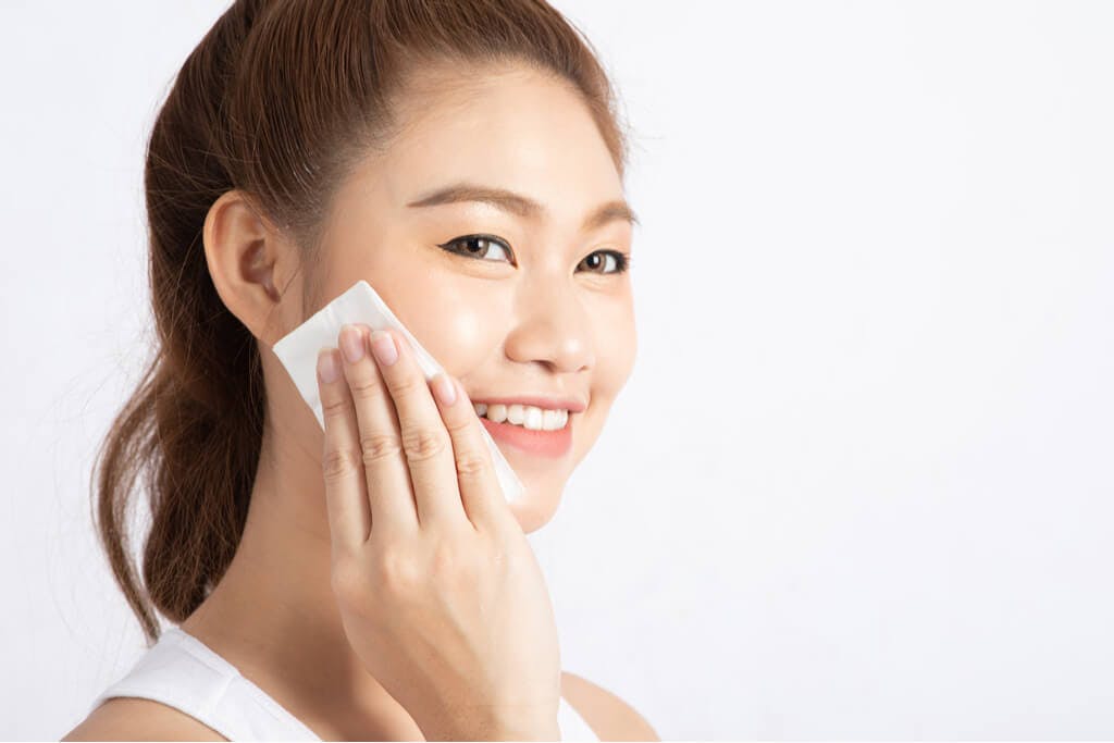 A woman using a pad to apply Japanese lotion to her face as she smiles into the camera