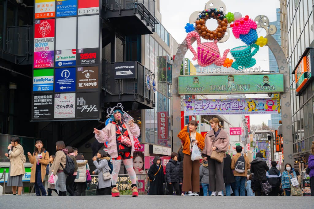 People in front of Harajuku's Takeshita Street with several desserts made of balloons above the takeshita street sign