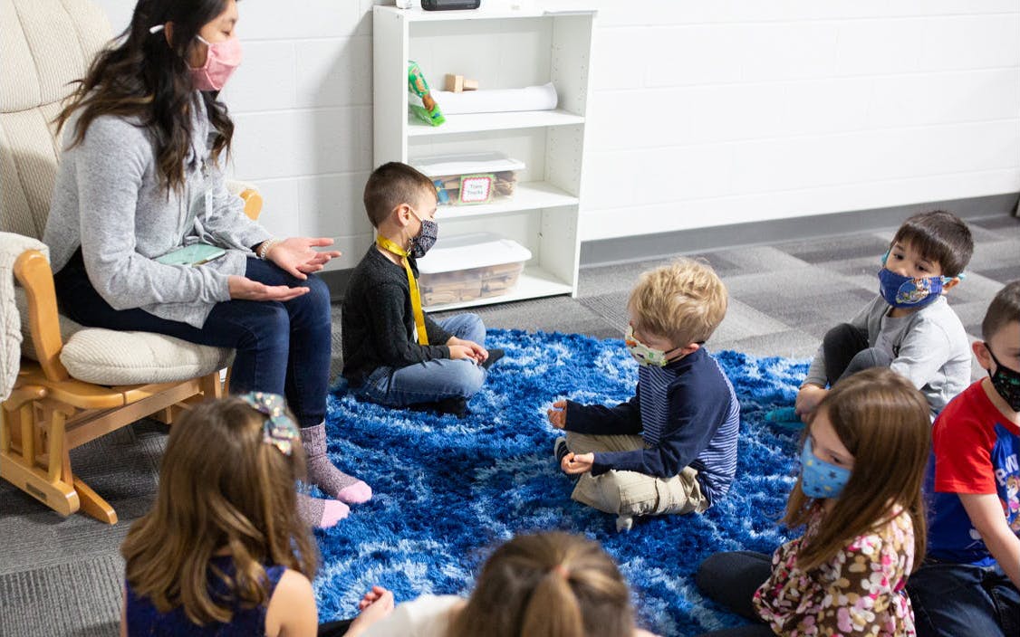 Four and five year old children praying on a large rug.