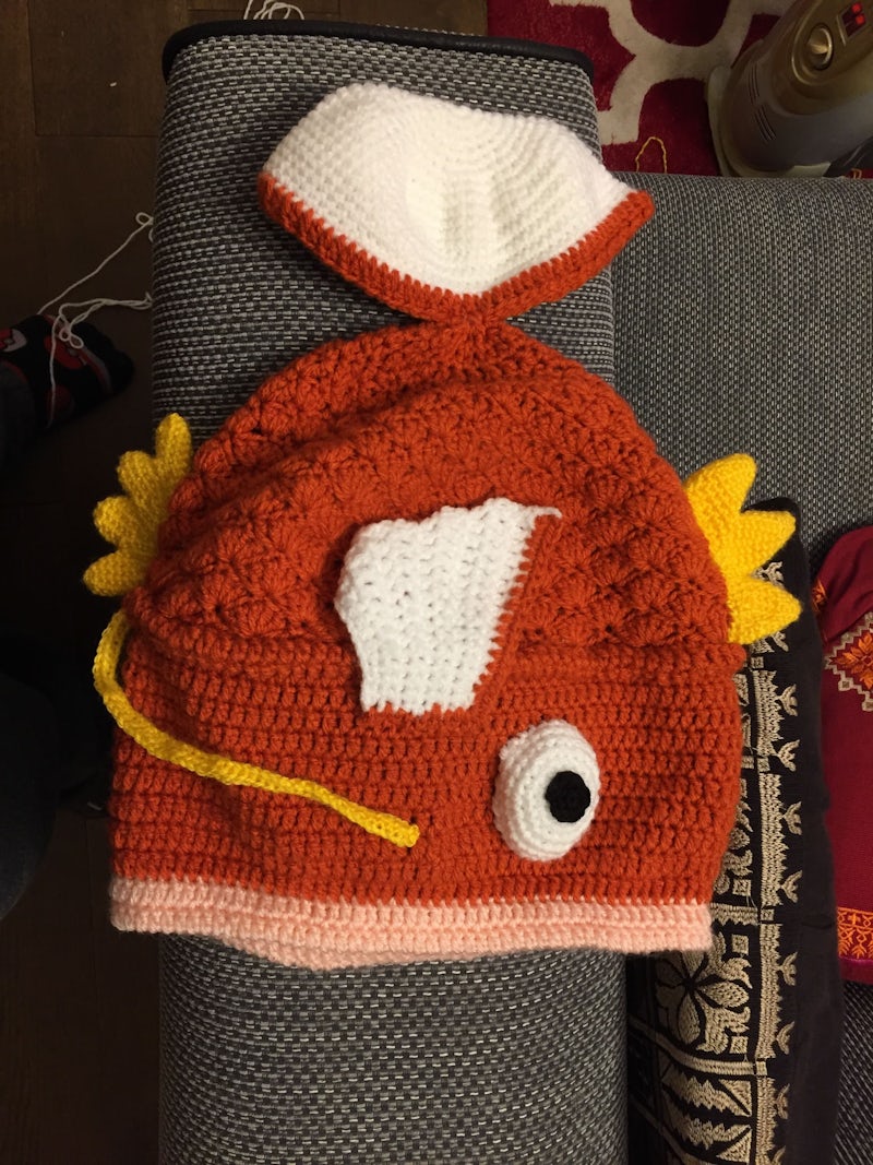 An intricate crocheted hat is laid out on a sofa's arm rest, the hat clearly resembles the magikarp pokemon.