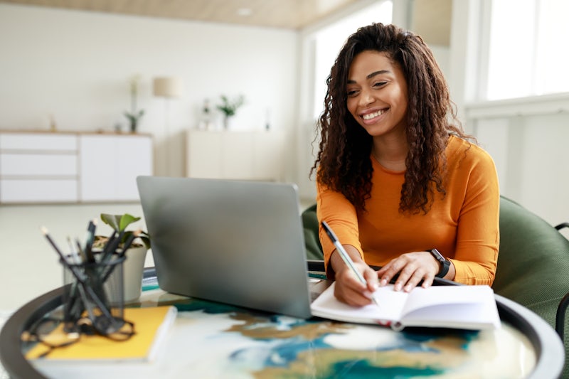 woman writing in notebook looking at her laptop