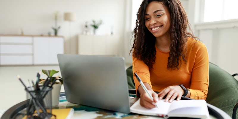 woman writing in notebook looking at her laptop