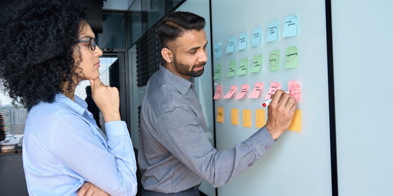 A woman and man writing on sticky notes on a board