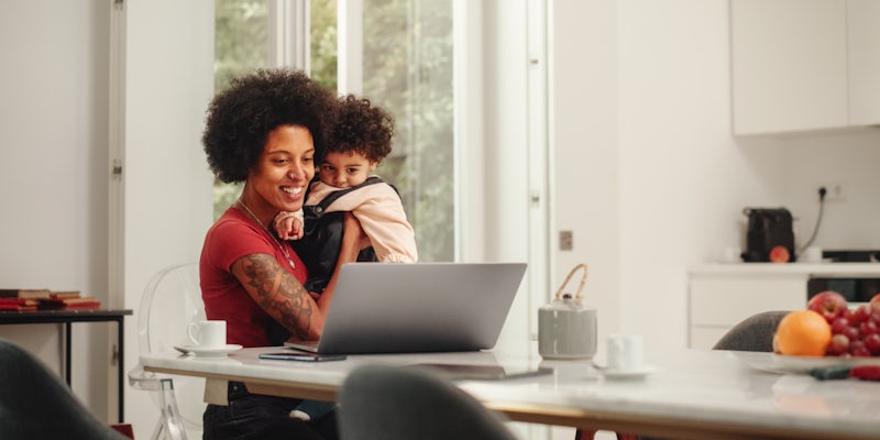 smiling woman sitting at her computer holing a toddler