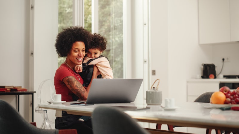 smiling woman sitting at her computer holing a toddler