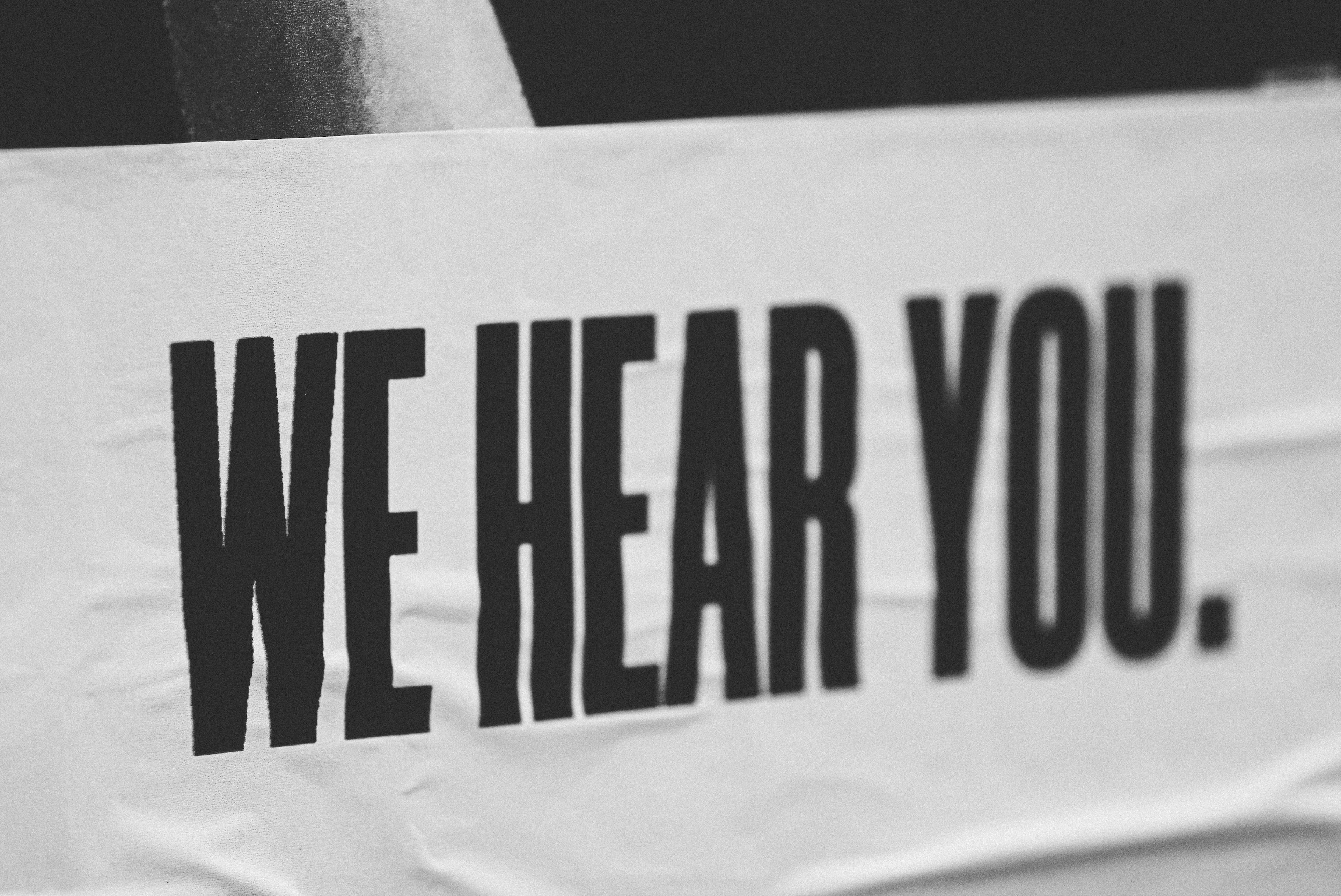 A black and white sign reading 'We hear you'. Credit: jon-tyson-unsplash