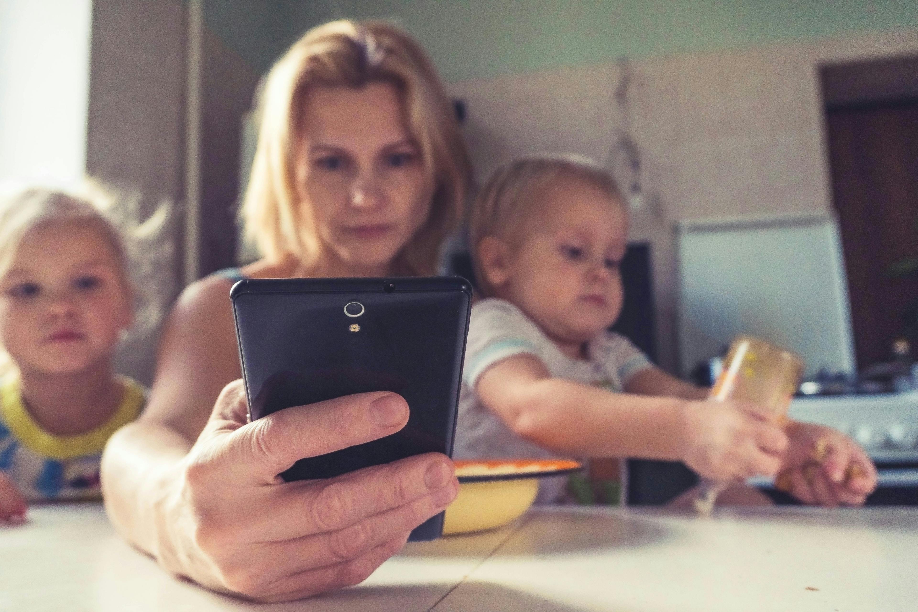 A mother reading her phone while sitting between two children. Credit: vitolda-klein-unsplash