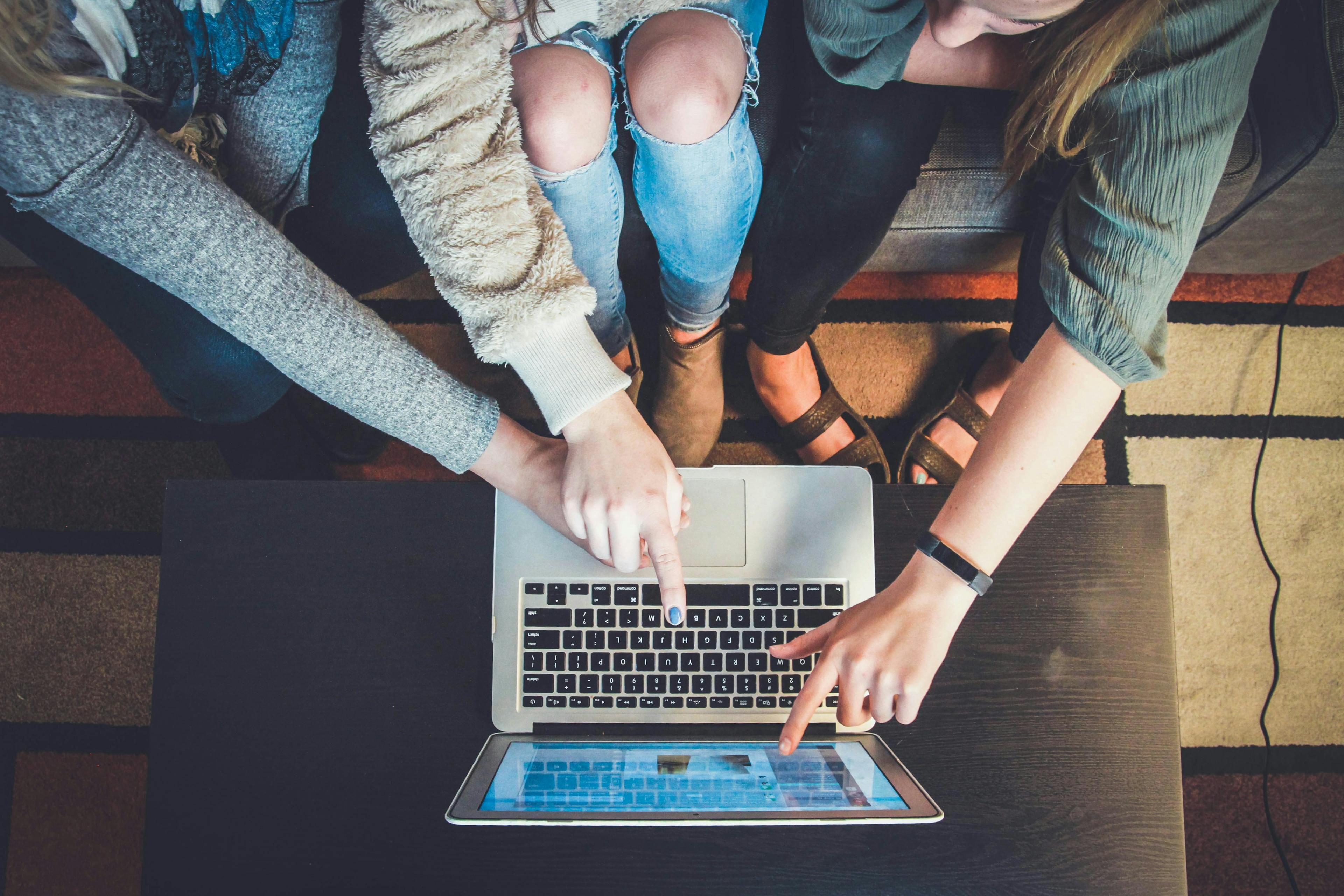 Aerial shot of three people pointing at a laptop. Credit: john-schnobrich-unsplash