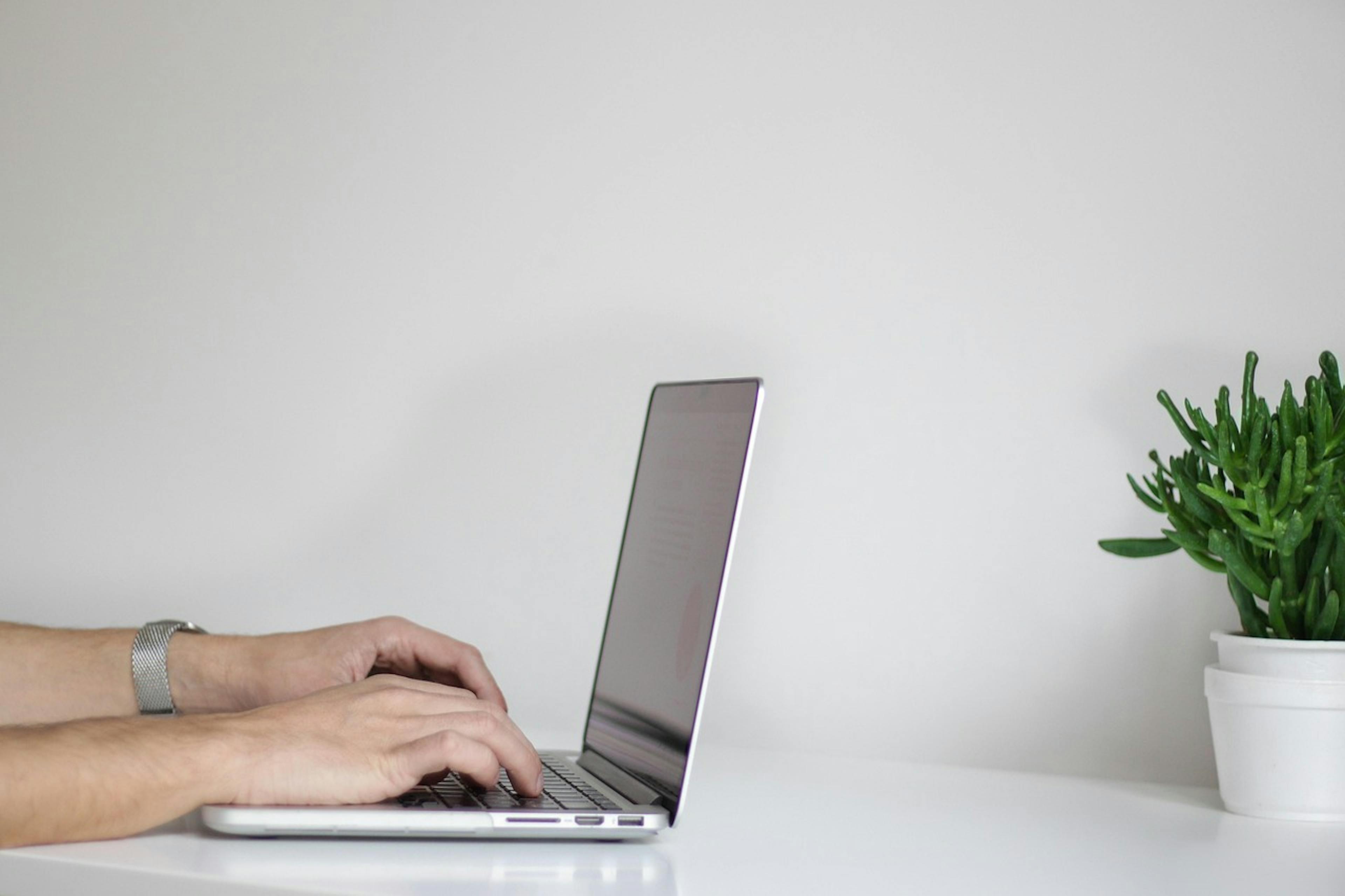 An image of someone's hands typing on a laptop - it is the main image for the article "Online Calendar: 8 Simple Apps That Make Organization Easy"