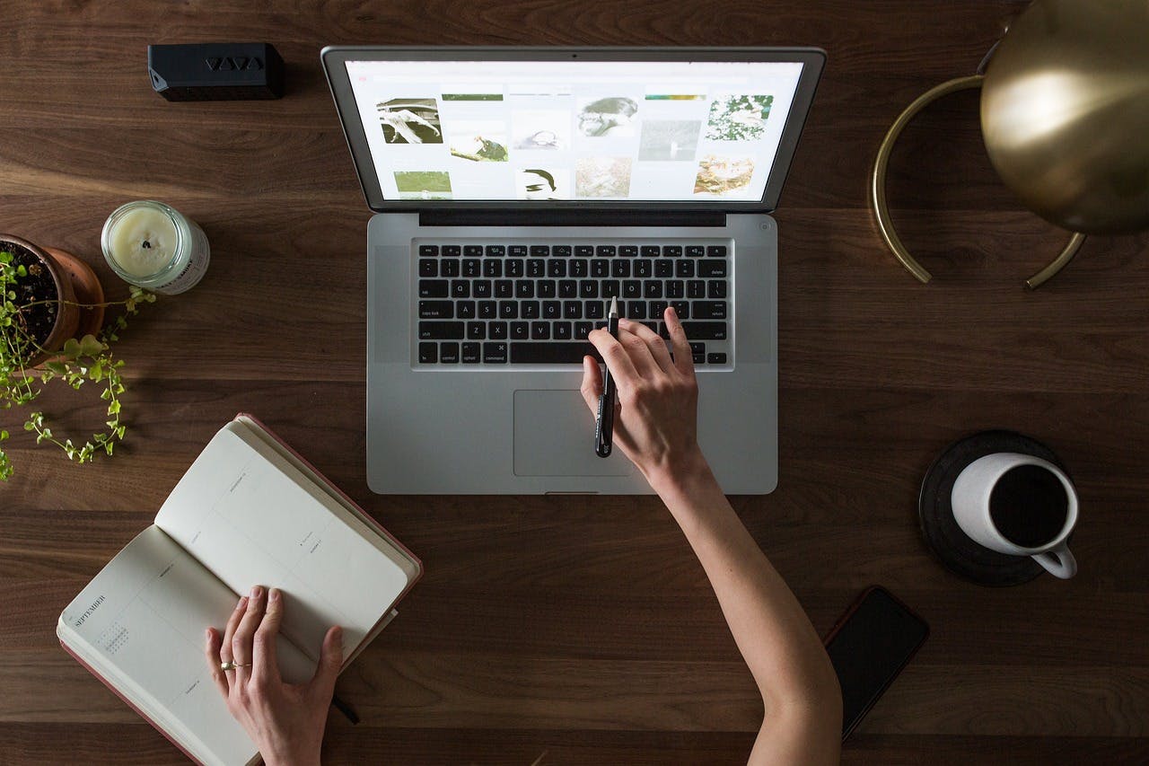 An image of someone typing on a laptop in one hand and flipping a notebook with the other - it is the main image for the article "Productivity Planner: 5 Proven Apps That Increase Productivity"