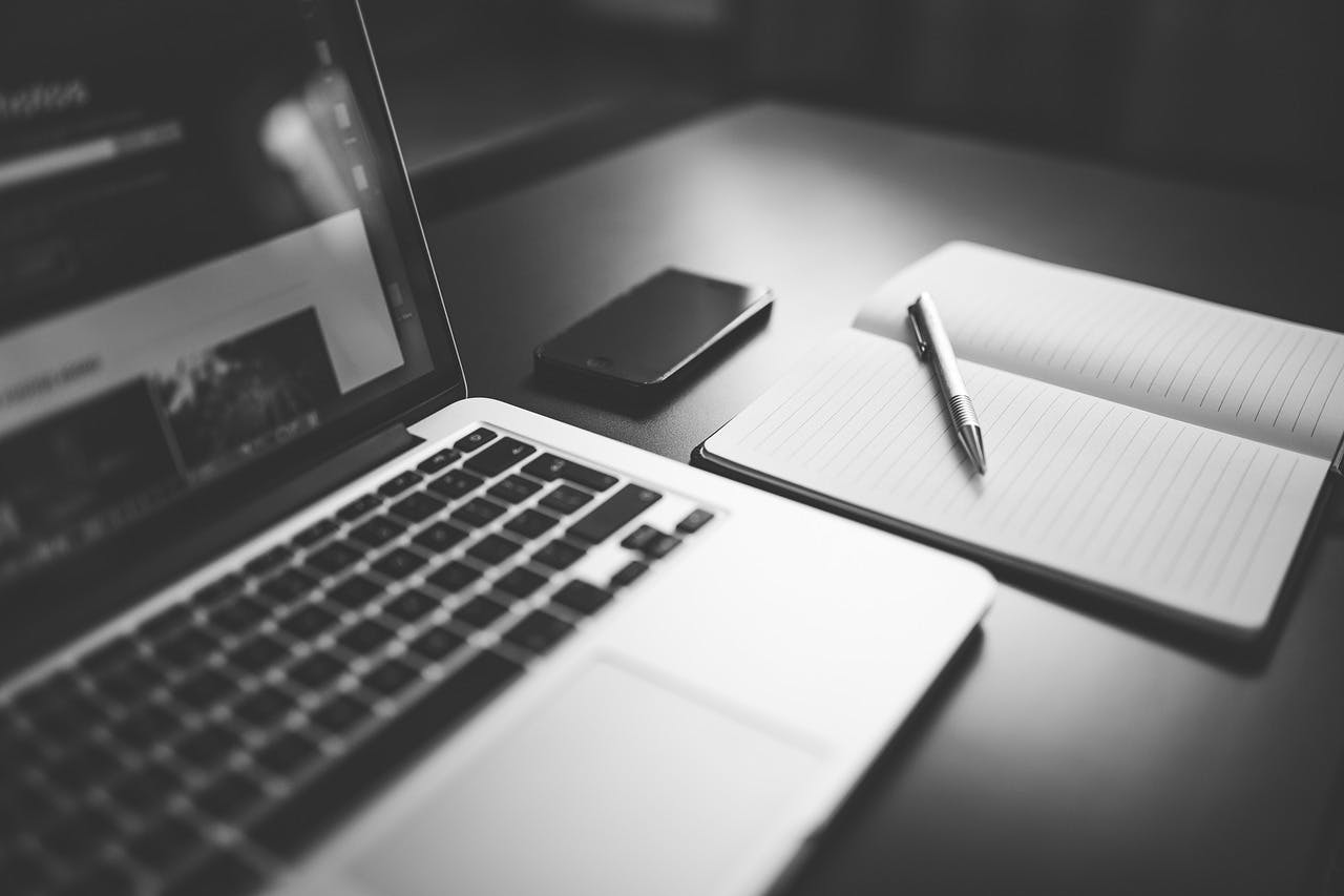 An image of a laptop next to a notebook - it is the main image for the article "5 Minute Journal: 7 Journals That Make Journaling Easy"