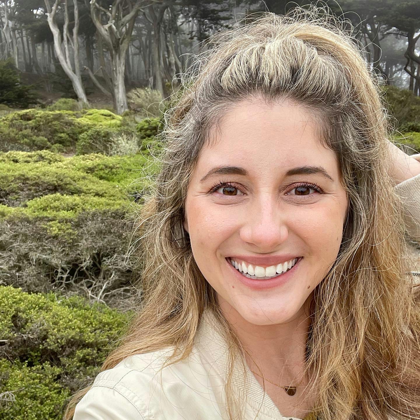 Profile photo of Courtney Brown, wearing a light yellow shirt, standing in front of a mossy landscape