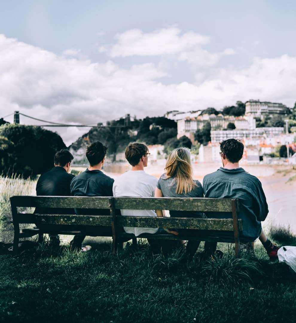 Group of people sat on a bench in Bristol overlooking the gorge with Clifton suspension bridge overhead.