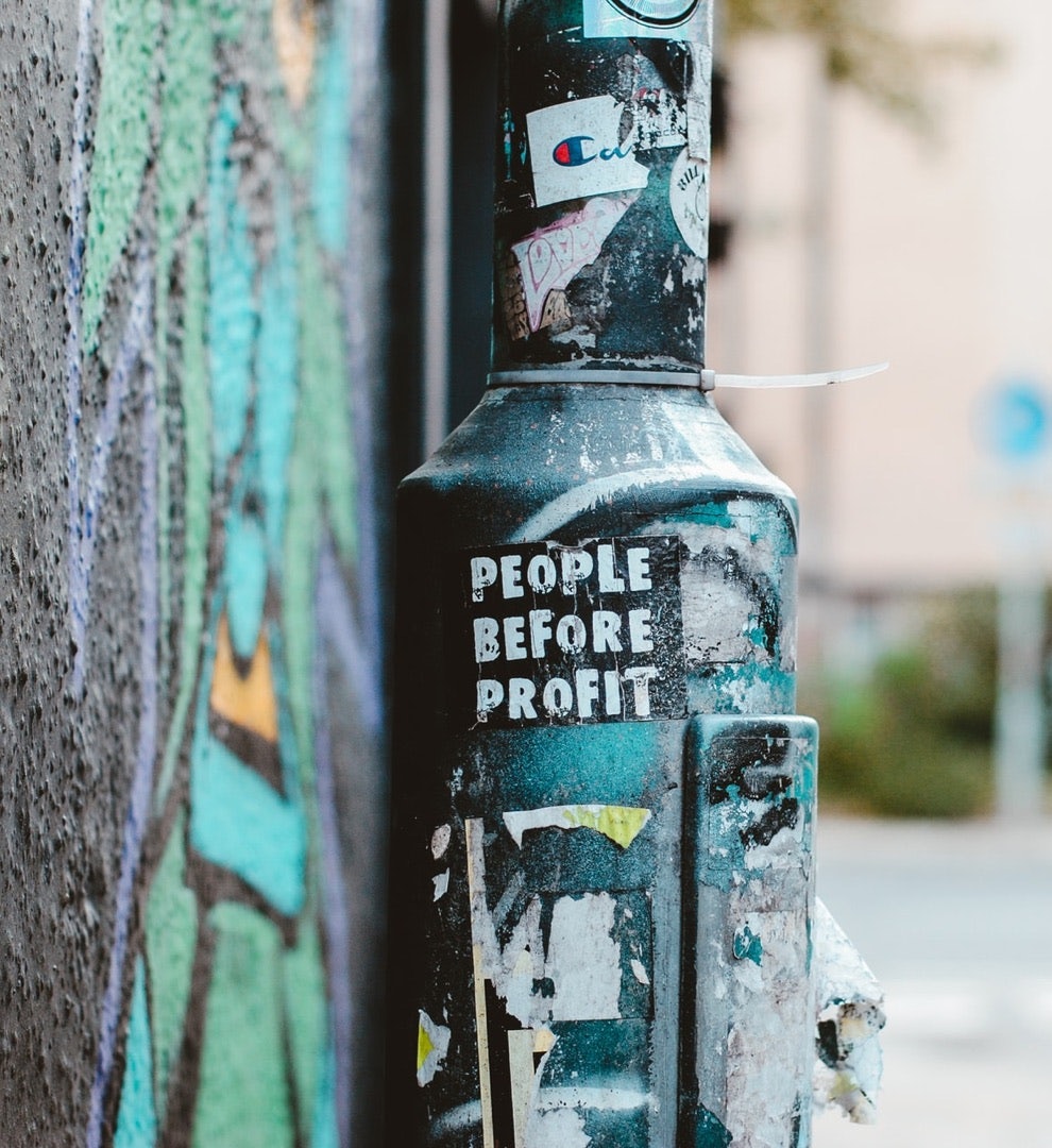 Image of a sticker on a lamppost that reads "people before profit".