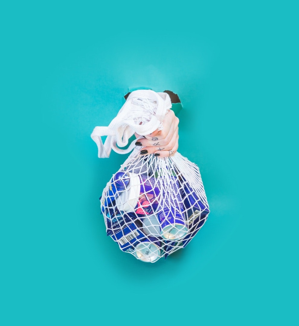Image of a hand holding a sustainable shopping bag full of rubbish.