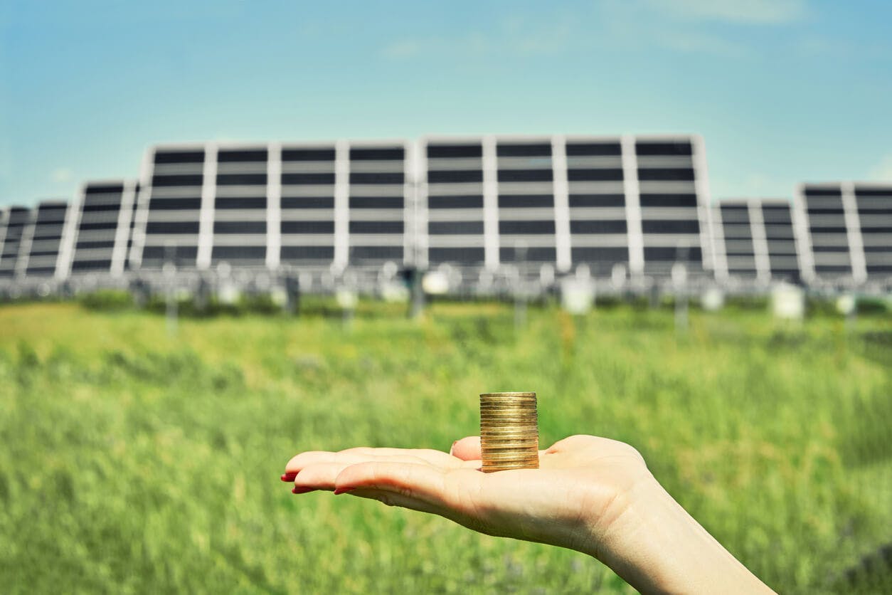 Mão segurando moedas na frente de placas solares simbolizando economia