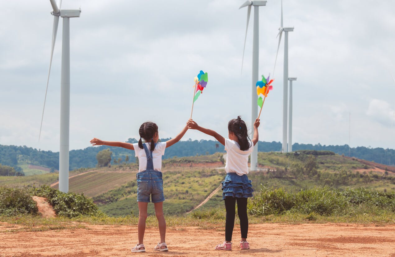 Duas meninas que brincam com cata-ventos e que olham o campo da turbina de vento junto