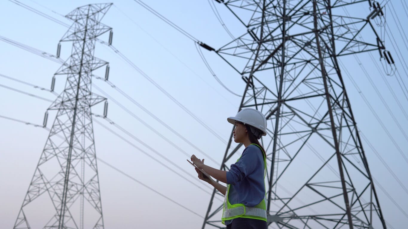 Engenheira elétrica trabalhando perto da torre de alta tensão.