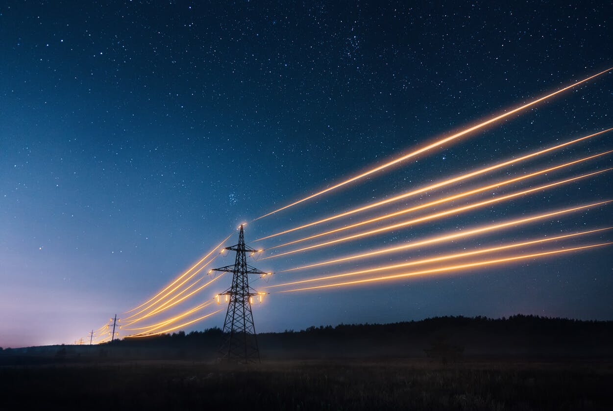 Torres de transmissão de eletricidade com fios laranjas brilhando contra o céu noturno.