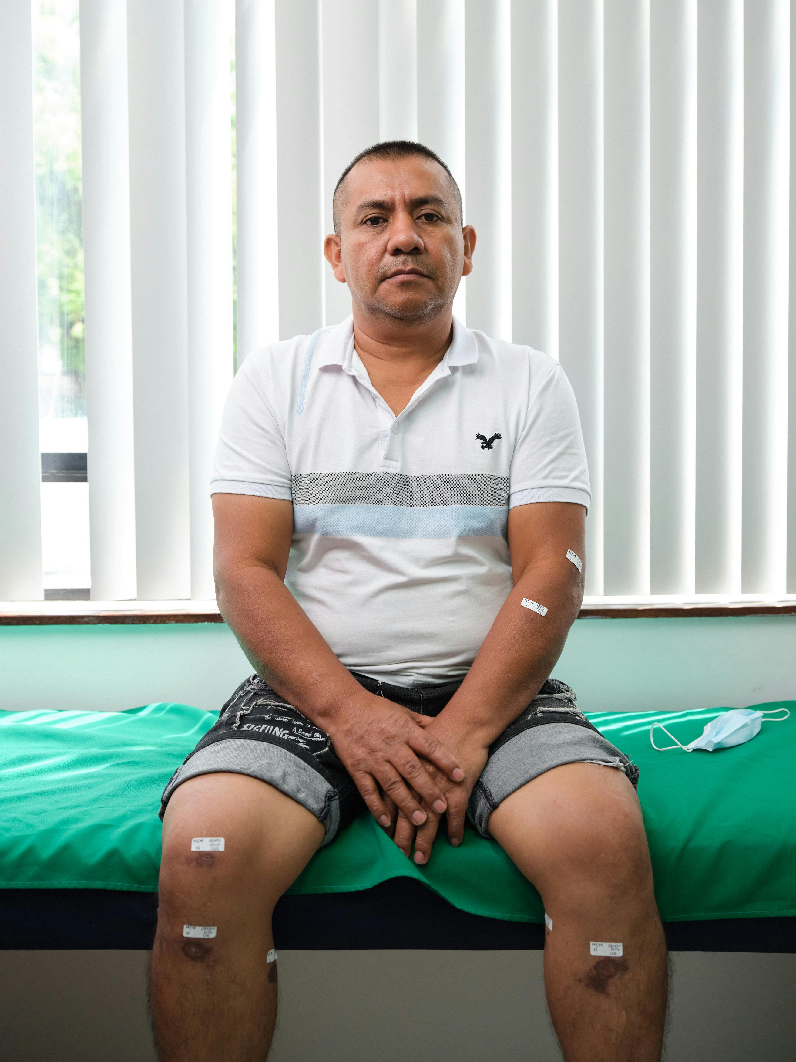 Ein Patient sitzt auf einem Bett. An seinen Oberschenkeln und Armen sind Pflaster zu sehen.