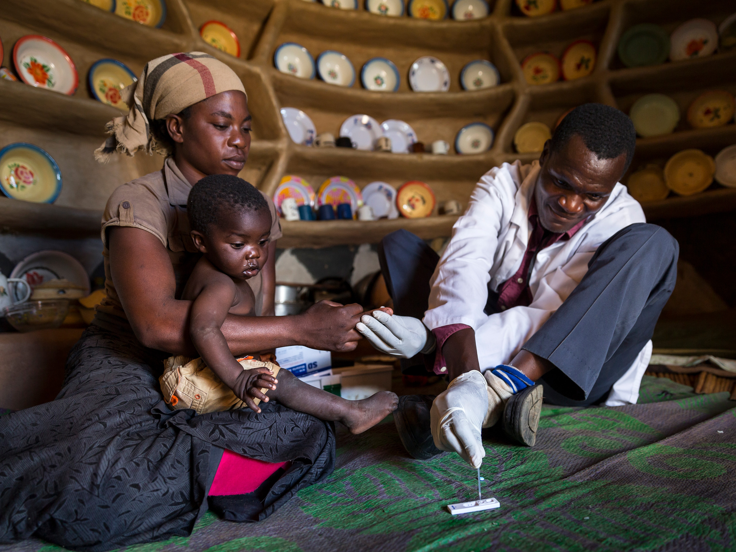 Eine medizinische Fachkraft in einem weißen Kittel kümmert sich um ein Kind, das von einer Frau gehalten wird.