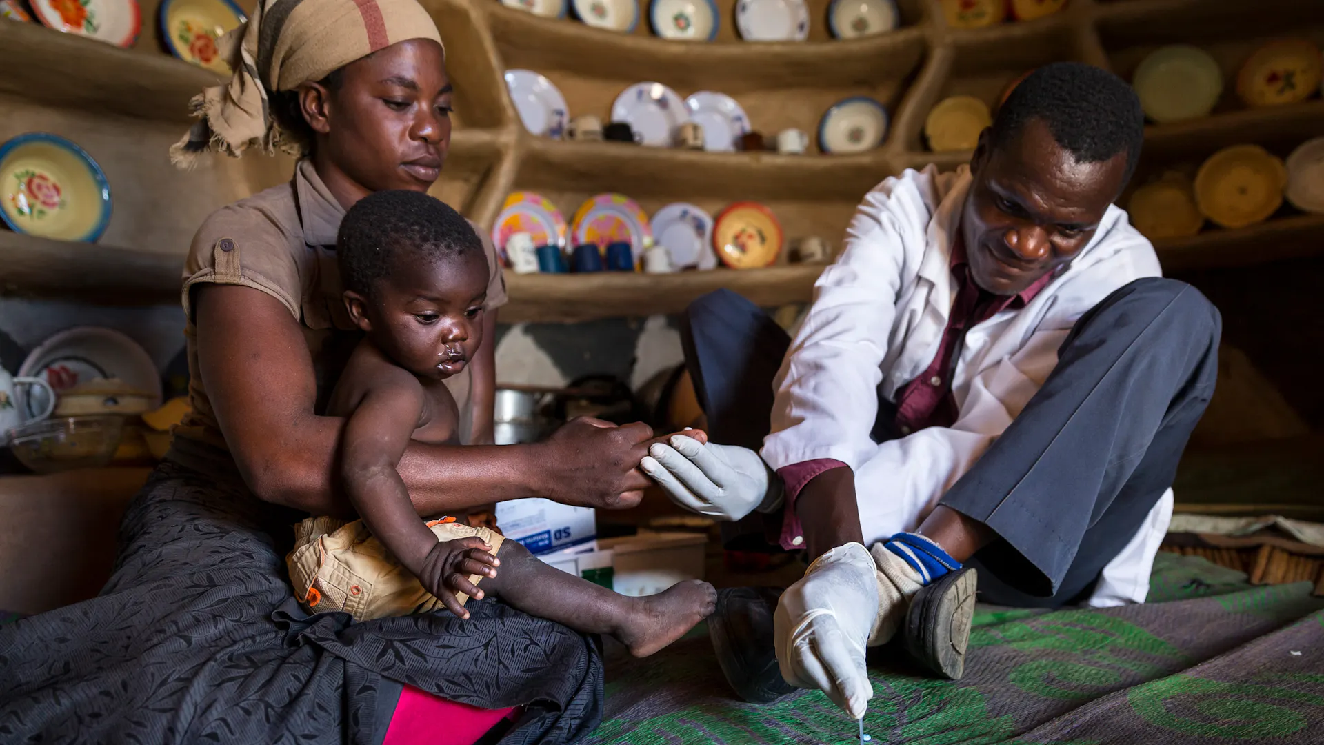 Eine medizinische Fachkraft in einem weißen Kittel kümmert sich um ein Kind, das von einer Frau gehalten wird.