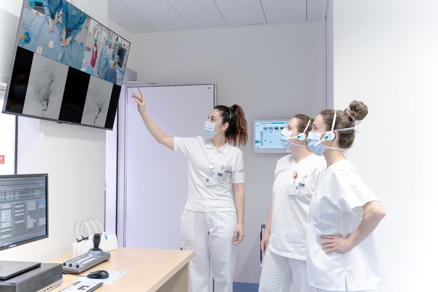 Three women follow the operation on the brain on a monitor.