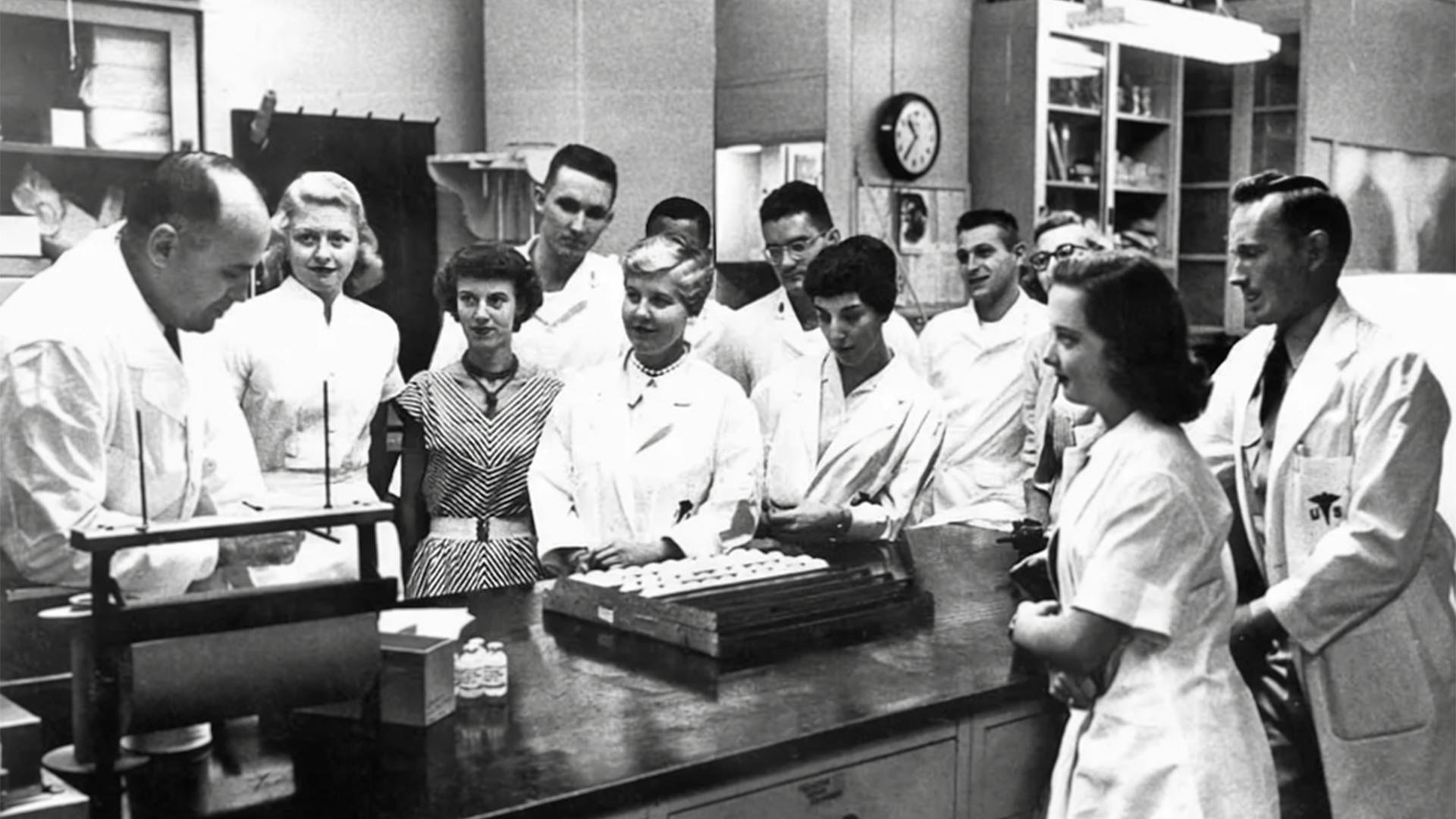 Schwarz-weiss-Aufnahme von Menschen im Labor, um wissenschaftliche Geräte stehend.