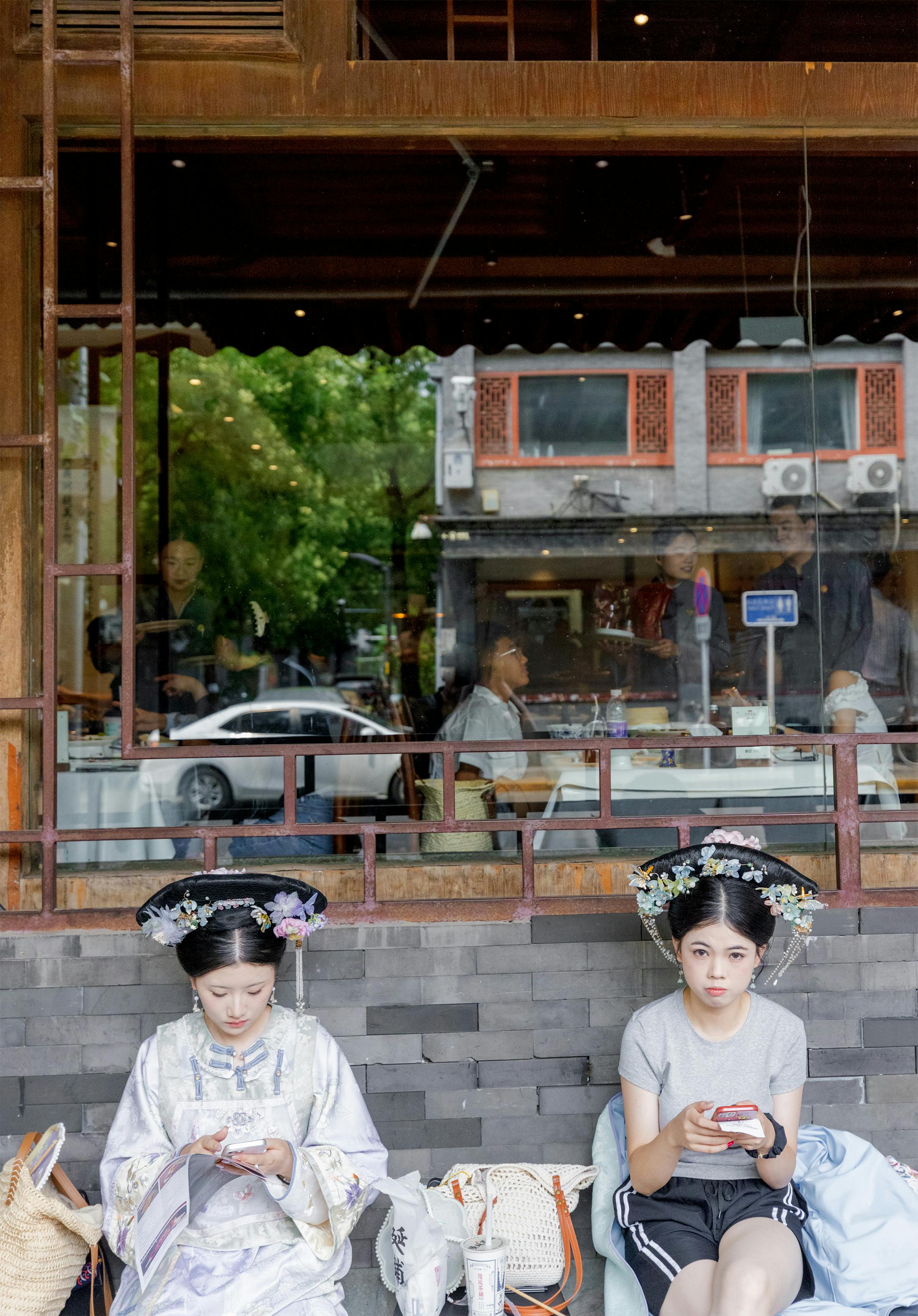Zwei Mädchen in Peking mit traditionellen Kopfbedeckungen und weiss geschminkter Haut.