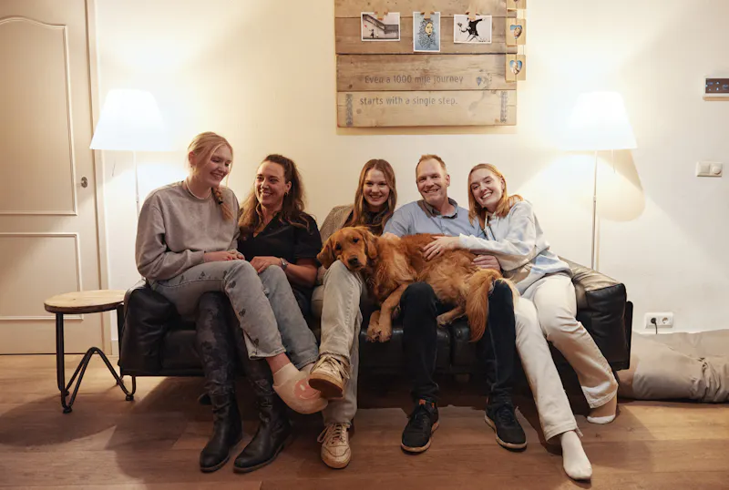 A family, mother and father with three grown up daughters sitting on their couch.