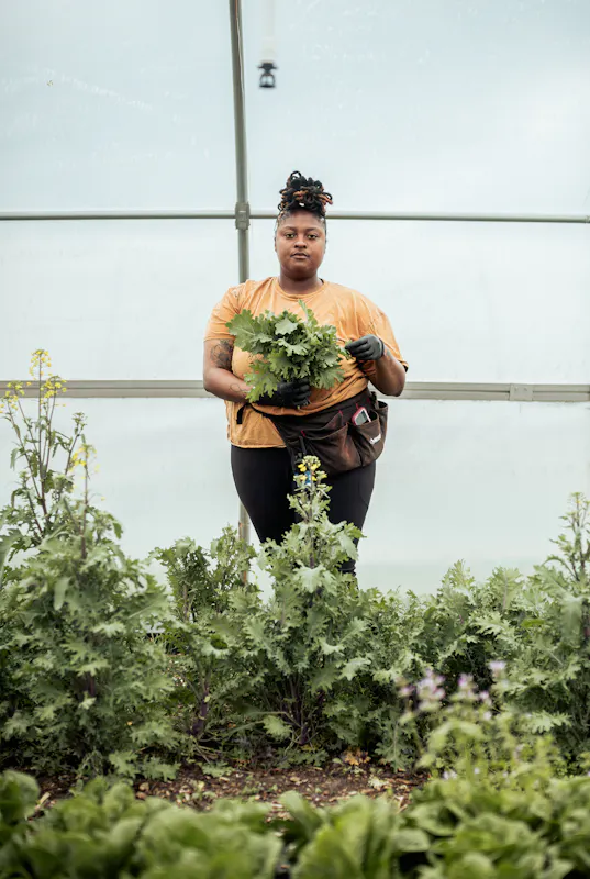 Woman standing in a greenhouse holding produce she just harvested.