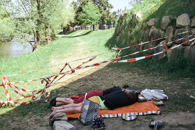 A couple sleeps on a picnic blanket next to the border fence. 