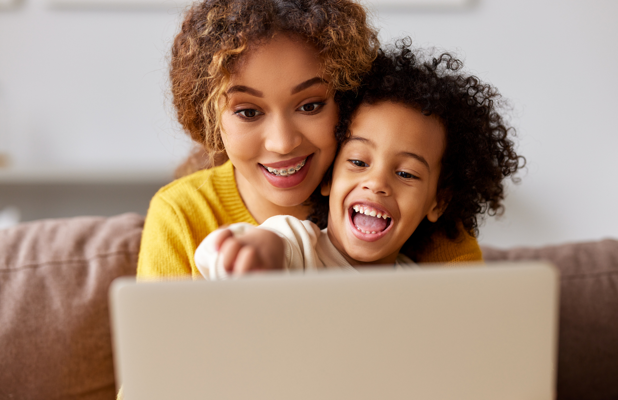 A young woman and child smile while looking at a laptop screen.