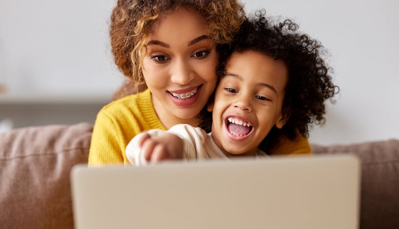A young woman and child smile while looking at a laptop screen.
