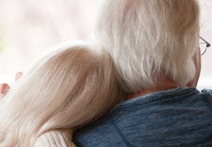 Two elderly individuals embracing, with their backs to the camera.