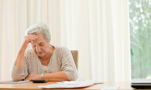 Woman sits at a desk looking at a calculator and rubbing her head.